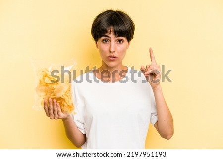 Young caucasian man holding crisps isolated on yellow background having an idea, inspiration concept.