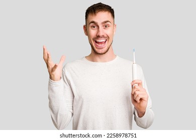 Young caucasian man holding an electric toothbrush isolated cut out receiving a pleasant surprise, excited and raising hands. - Shutterstock ID 2258978751