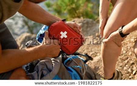 Young caucasian man holding first aid kit for healing injured woman knee during hiking in summer nature, widescreen, cropped. Hiking, travel outdoor, recreation and active adventure concept