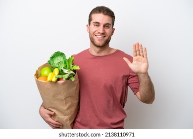 Young Caucasian Man Holding A Grocery Shopping Bag Isolated On White Background Saluting With Hand With Happy Expression