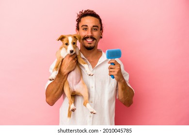 Young Caucasian Man Holding His Puppy And Dog Brush Isolated On Pink Background