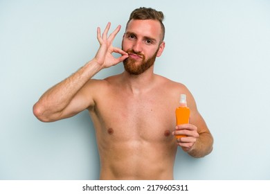 Young Caucasian Man Holding Solar Cream Isolated On Blue Background With Fingers On Lips Keeping A Secret.