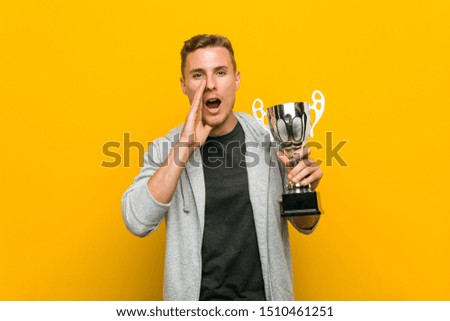 Young caucasian man holding a trophy shouting excited to front.