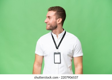 Young caucasian man with ID card isolated on green chroma background looking side