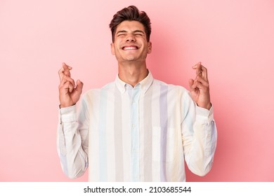 Young caucasian man isolated on pink background crossing fingers for having luck