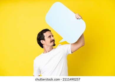 Young Caucasian Man Isolated On Yellow Background Holding An Empty Speech Bubble