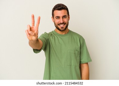 Young caucasian man isolated on white background showing victory sign and smiling broadly.