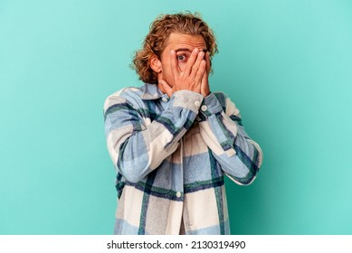 Young Caucasian Man Isolated On Blue Background Blink Through Fingers Frightened And Nervous.