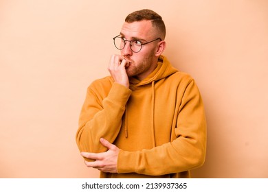 Young caucasian man isolated on beige background biting fingernails, nervous and very anxious.