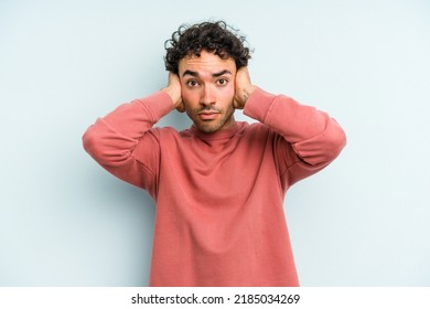 Young caucasian man isolated on blue background covering ears with hands trying not to hear too loud sound. - Shutterstock ID 2185034269