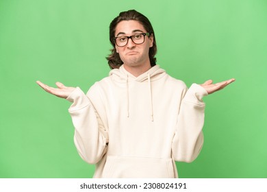 Young caucasian man isolated on green chroma background having doubts while raising hands - Shutterstock ID 2308024191