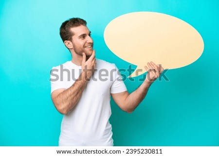 Young caucasian man isolated on blue background holding an empty speech bubble and pointing it