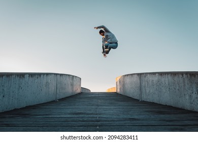 Young caucasian man in jeans and hoodie jumping on concrete bridge. Mid air parkour pose in city environment and clear sky