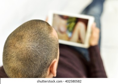 a young caucasian man lying on the couch watches porn in his tablet computer