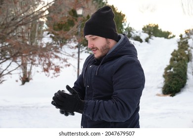 Young Caucasian Man Making A Snowball In A Park.