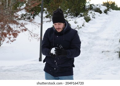 Young Caucasian Man Making A Snowball In A Park