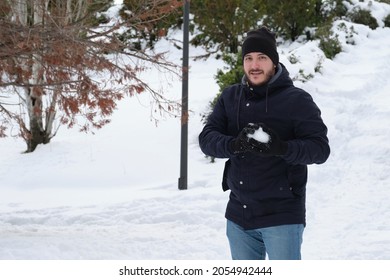 Young Caucasian Man Making A Snowball In A Park