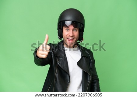 Young caucasian man with a motorcycle helmet isolated on green chroma background with thumbs up because something good has happened