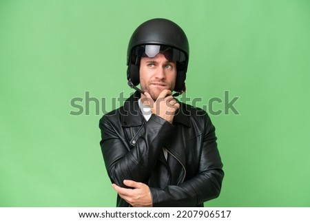 Young caucasian man with a motorcycle helmet isolated on green chroma background having doubts and thinking