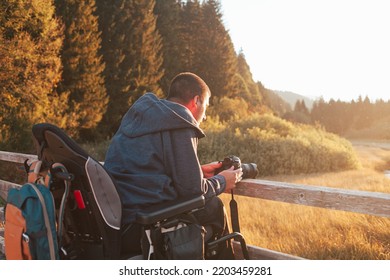 Young Caucasian man on wheelchair on a wooden bridge, using a camera to take a photo of beautiful mountain nature - Powered by Shutterstock