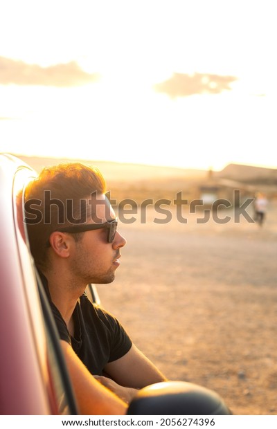 Young\
caucasian man outside a window car at a dry landscape while sunset\
at Bardenas Reales, Navarra, Basque\
Country.