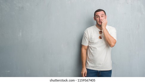 Junge Kaukasier auf grauem Grunge Wand mit Sonnenbrille, gestresst und nervös mit Händen auf Mund beißenden Nägeln. Angstprobleme.