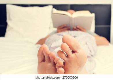 A Young Caucasian Man In Pajamas Reading A Book In Bed