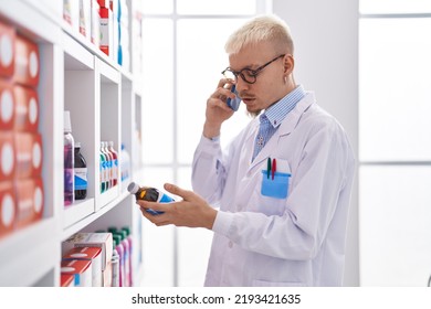 Young Caucasian Man Pharmacist Talking On Smartphone Holding Medicine Bottle At Pharmacy