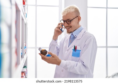 Young Caucasian Man Pharmacist Talking On Smartphone Holding Medicine Bottle At Pharmacy