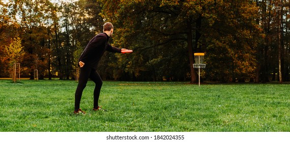 Young caucasian man playing disc golf on autumn play course with basket
