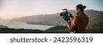 A young Caucasian man with a professional camera in his hands on a mountain by the sea.  The operator holds a video camera, shoots a sunset landscape, mountains, sea, setting sun
