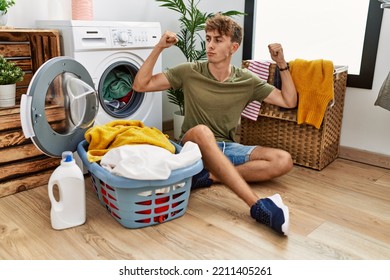 Young Caucasian Man Putting Dirty Laundry Into Washing Machine Showing Arms Muscles Smiling Proud. Fitness Concept. 