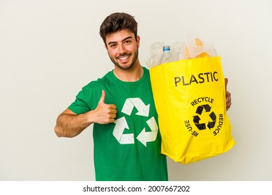 Young caucasian man recycling plastic isolated on white background smiling and raising thumb up