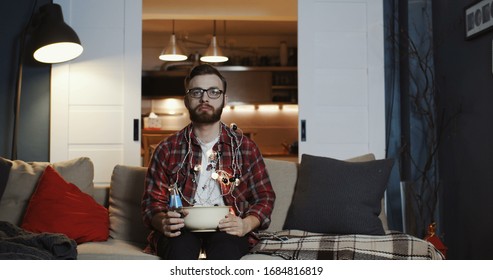 Young Caucasian Man Is Sad And Depressed Watching Movie At Home, Eating Snacks Alone At Empty House Party Slow Motion.