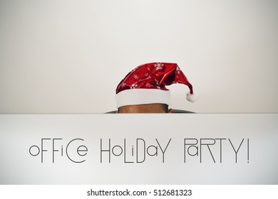 A Young Caucasian Man With A Santa Hat, Behind The Screen Of His Computer Where You Can Read Office Holiday Party, Sitting At His Office Desk