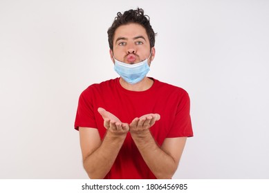 Young Caucasian Man With Short Hair Wearing Medical Mask Standing Over Isolated White Background Sending Blow Kiss With Pout Lips And Holding Palms To Send Air Kiss.