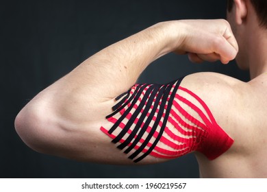 Young Caucasian Man Showing Bicep With Kinesiology Medical Tape Applied To Relieve Pain On Dark Background, Back View, Closeup