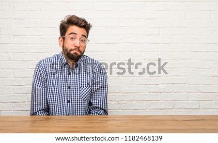 Young caucasian man sitting doubting and shrugging shoulders, concept of indecision and insecurity, uncertain about something