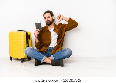 Young Caucasian Man Sitting Holding A Passport And A Suitcase Isolated Feels Proud And Self Confident, Example To Follow.