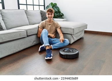 Young Caucasian Man Sitting At Home By Vacuum Robot Smiling Happy Pointing With Hand And Finger 