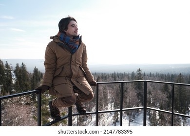 Young Caucasian man sitting relaxed on protection fence at observation deck on mountain top looking away
