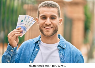 Young Caucasian Man Smiling Happy Holding Colombian Pesos At The City.