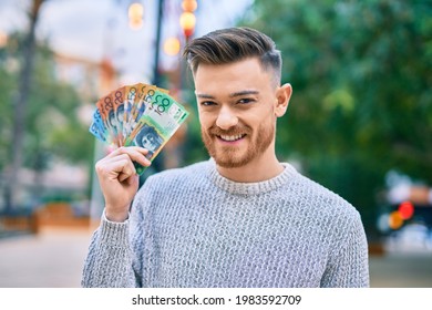 Young caucasian man smiling happy holding australian dollars at the park.