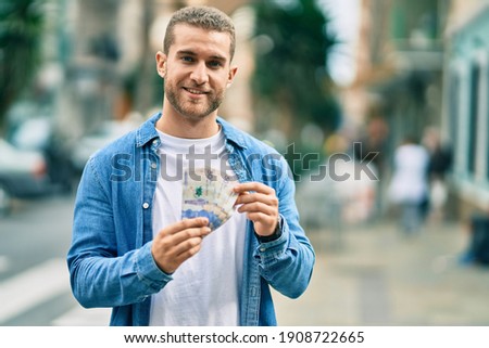 Young caucasian man smiling happy counting colombian pesos at the city.