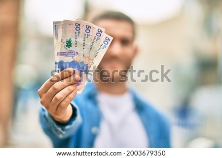 Young caucasian man smiling happy holding colombian pesos at the city.