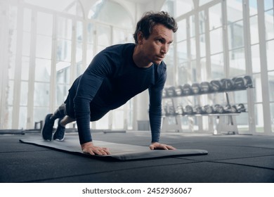 Young caucasian man in sportswear in plank position while doing push-ups on exercise mat at gym - Powered by Shutterstock