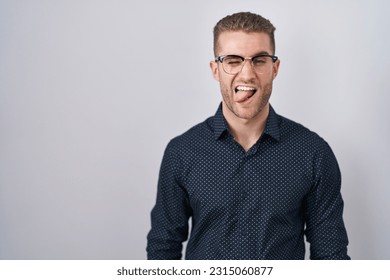 Young caucasian man standing over isolated background sticking tongue out happy with funny expression. emotion concept. 