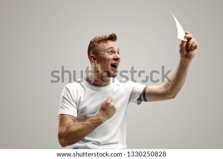 Young caucasian man with a surprised happy expression won a bet on gray studio background. Human facial emotions and betting concept