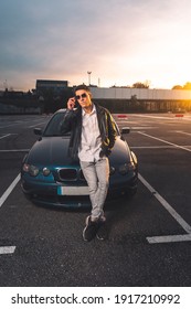 Young Caucasian Man Using A Smartphone With A Sports Car Behind