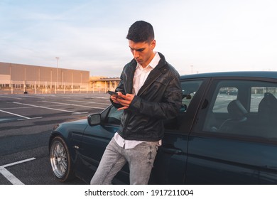 Young Caucasian Man Using A Smartphone With A Sports Car Behind